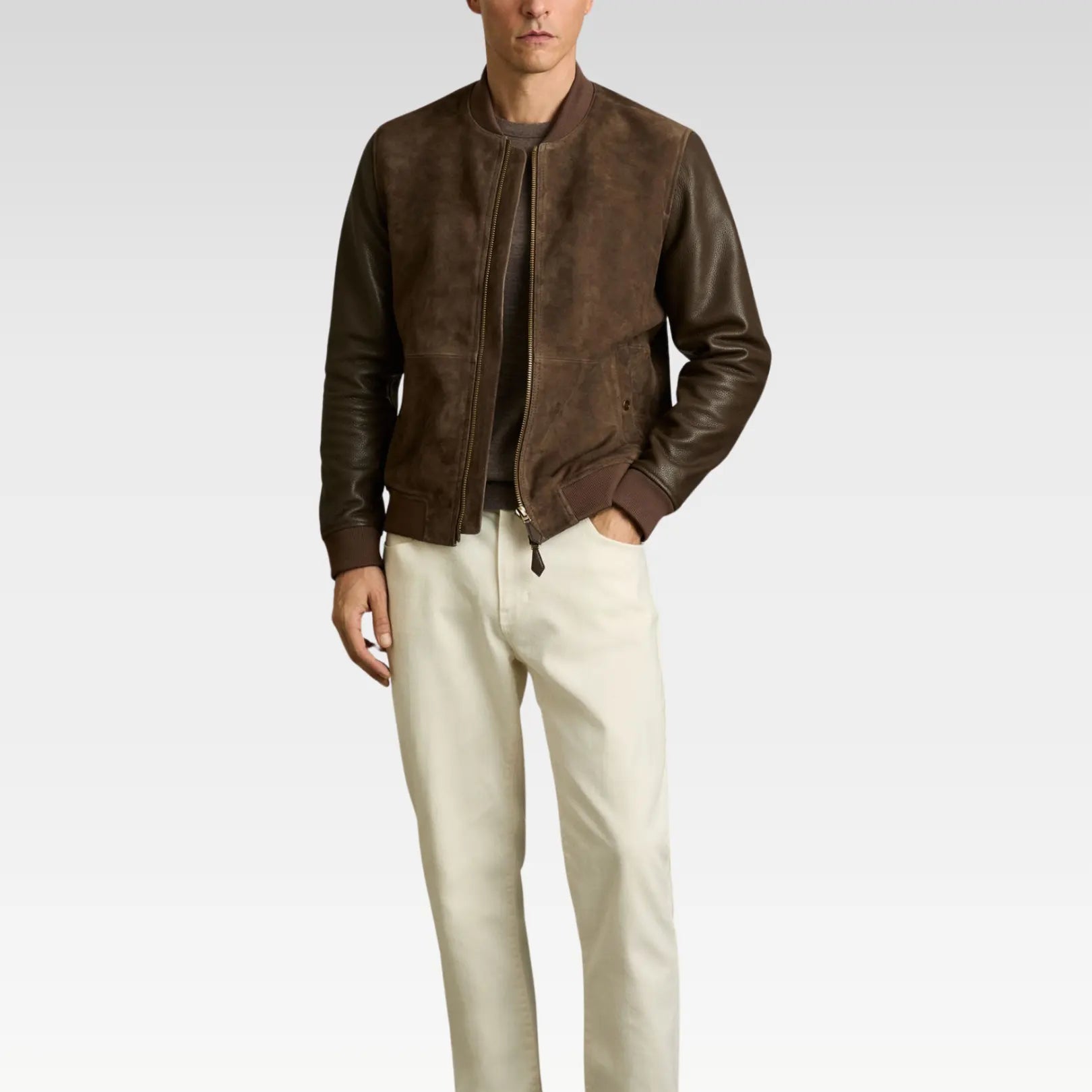 Man wearing a brown leather jacket and white pants on a plain background
