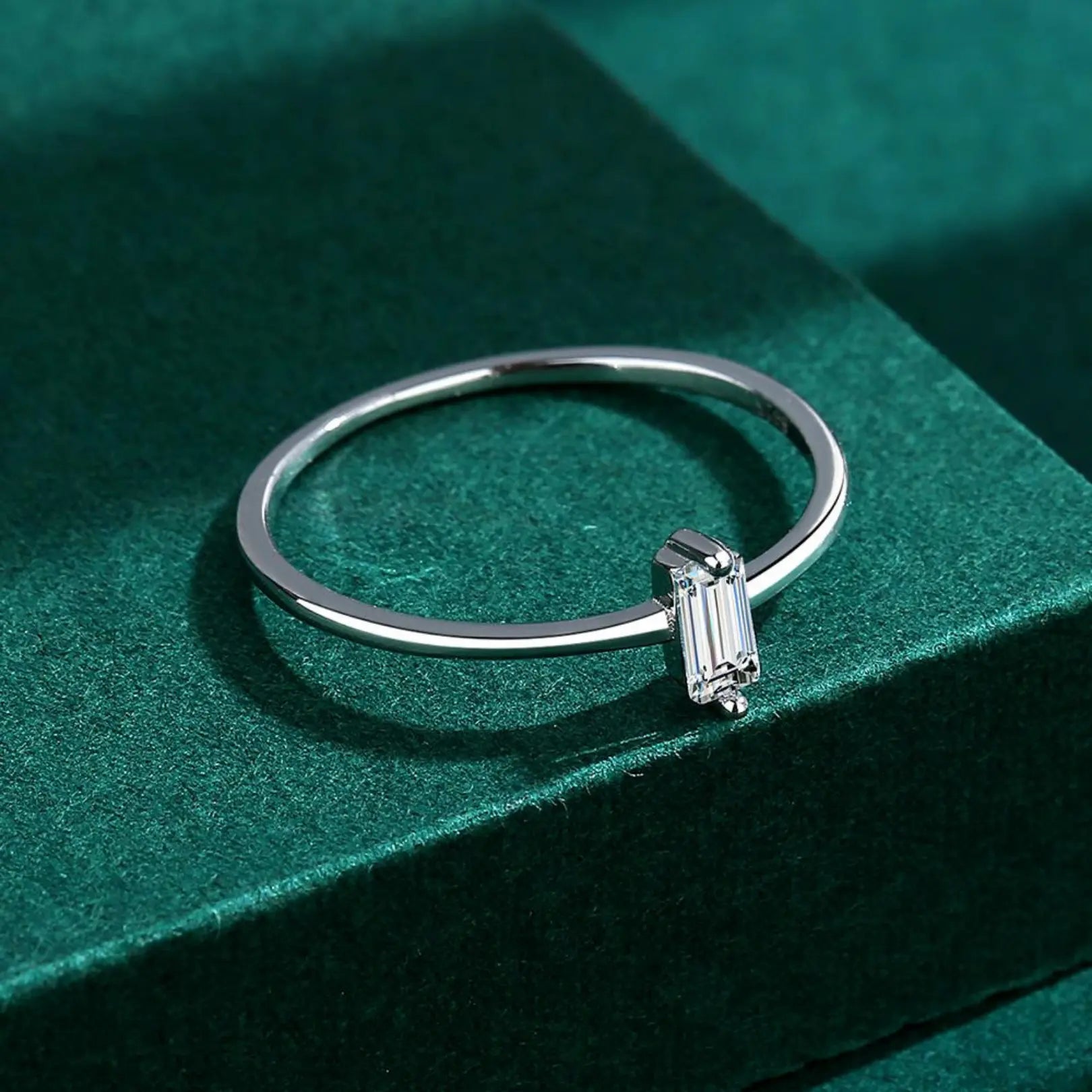  Minimalist silver ring featuring a vertical baguette-cut white zircon, displayed on a green background.