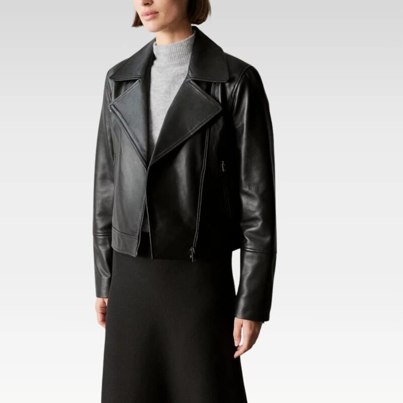 Close-up of black leather biker jacket highlighting notched lapels, silver hardware, and tailored fit, worn over grey turtleneck.