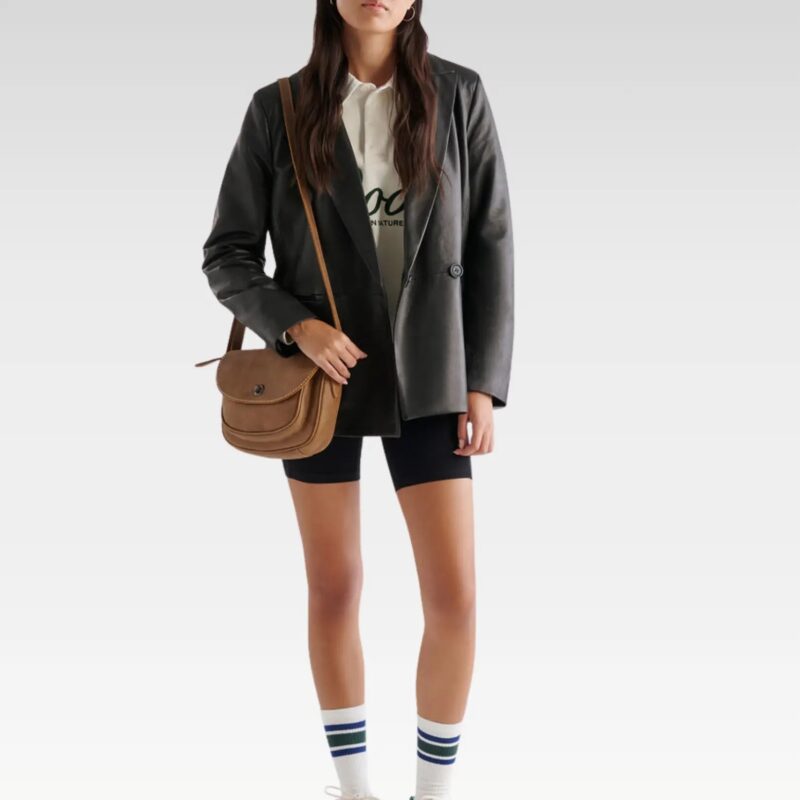Model wearing the women’s black leather double breasted blazer styled over a white blouse and shorts, showcasing a modern city-chic look with functional front pockets.