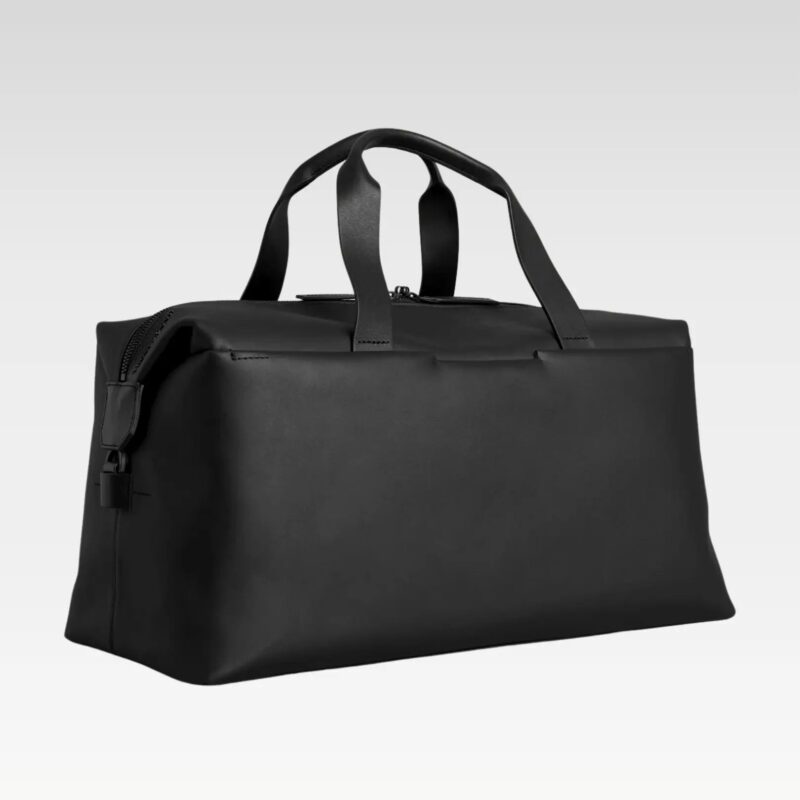Sleek black full-grain leather duffle bag standing upright, featuring detachable shoulder strap and magnetic exterior pockets.