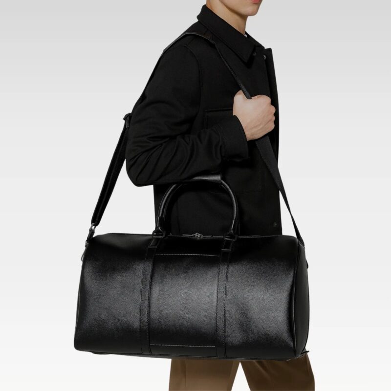 Black Monte leather duffel bag worn over the shoulder, demonstrating adjustable strap and roomy interior for travel essentials.