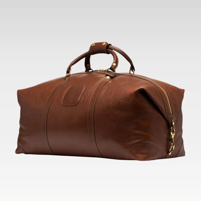 Side-angle view of the Rogue premium full-grain leather duffel bag highlighting its brass hardware and classic finish.
