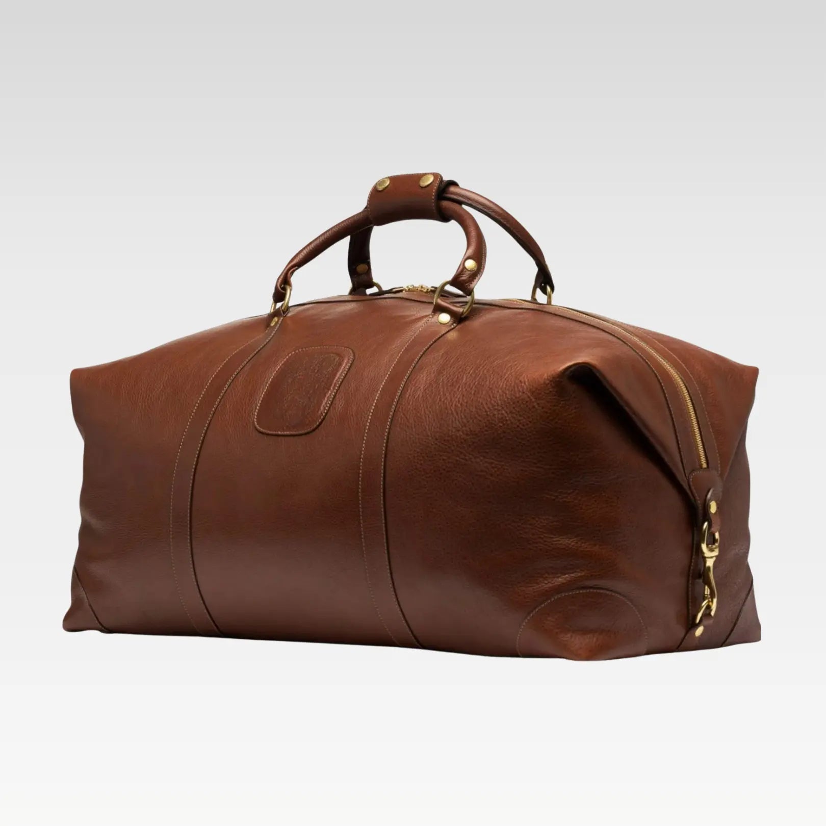 Side-angle view of the Rogue premium full-grain leather duffel bag highlighting its brass hardware and classic finish.