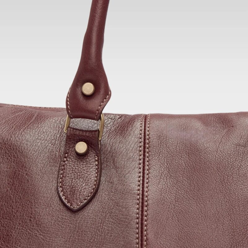 Close-up of the Saddler duffle bag’s double-stitched leather strap and hardware, showing durable craftsmanship and premium material.