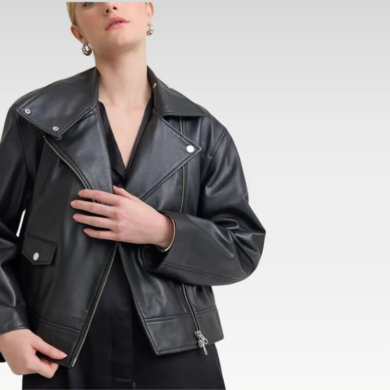 Model wearing the Sasha biker black leather jacket unzipped over a neutral top, showing the metallic zips, press-stud lapels, and relaxed cropped fit.